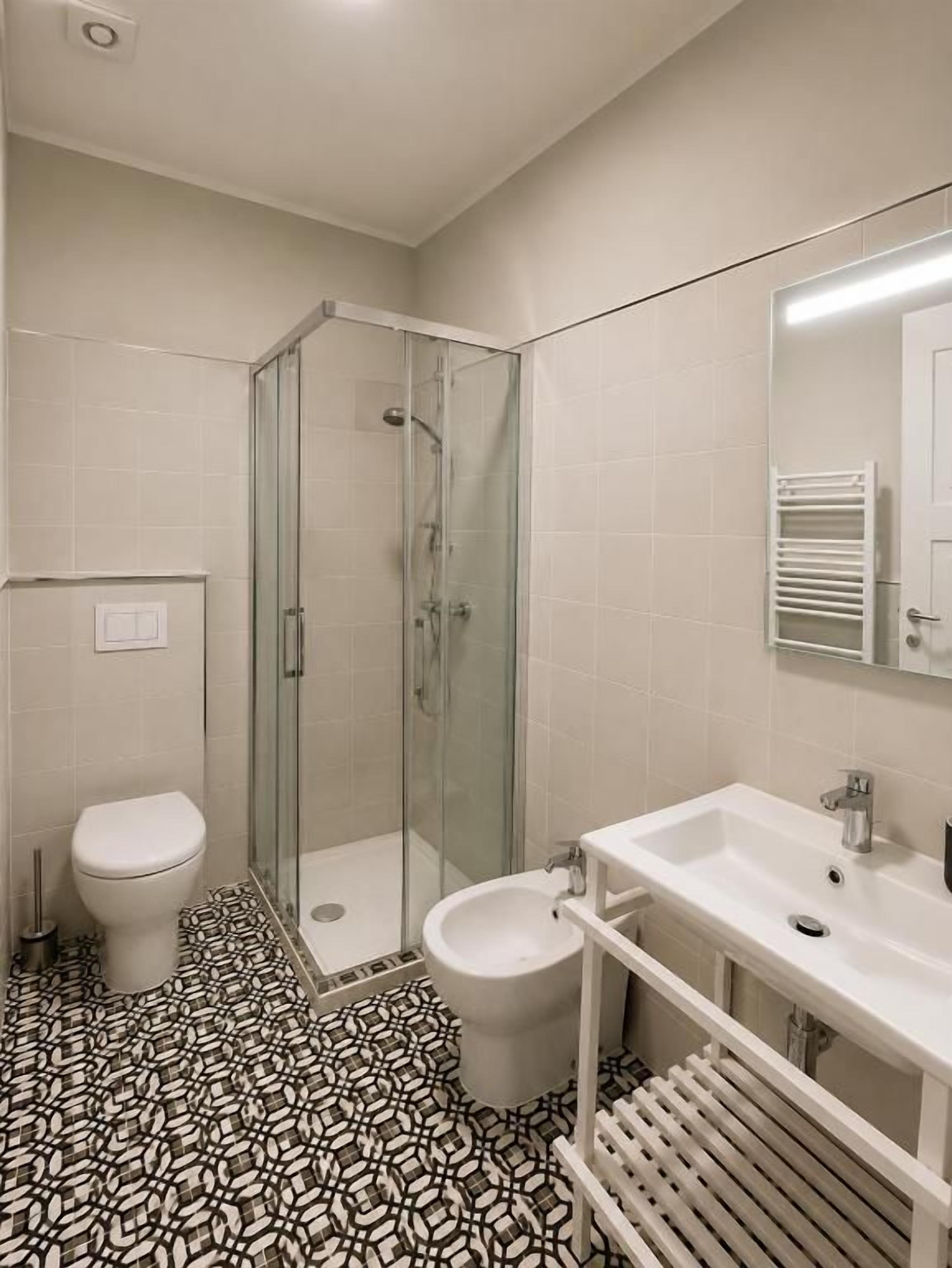Un baño con ducha de vidrio, inodoro, bidé y lavamanos con espejo.