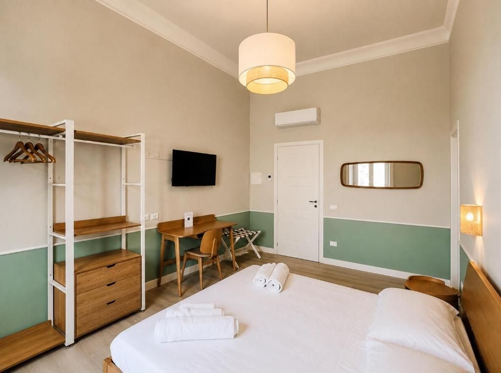 A hotel room with a bed, a desk, a chair, a wardrobe, a television, and a mirror.