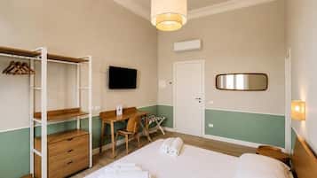 A hotel room with a bed, a desk, a chair, a wardrobe, a television, and a mirror.