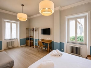 Una habitación de hotel con cama, escritorio, silla, televisor y armario.