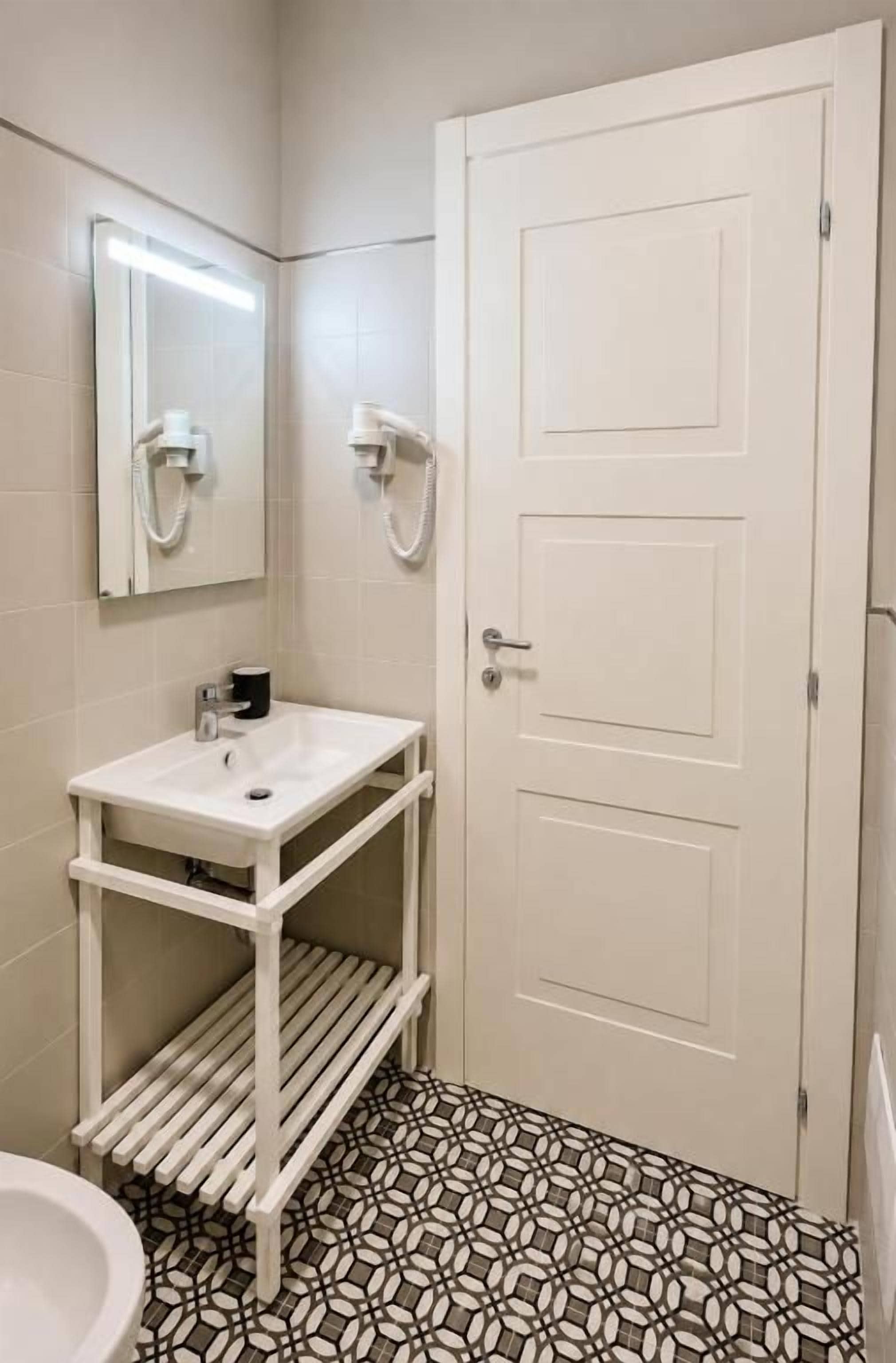 Un baño con lavamanos blanco, un espejo, inodoro y piso estampado.