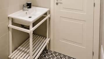 Un baño con lavamanos blanco, un espejo, inodoro y piso estampado.