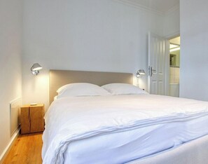 A neatly made bed in a hotel room with a wooden nightstand and two wall-mounted lamps. - Country House on the Riverbank, Apartment 1 (Heiligenhafen)