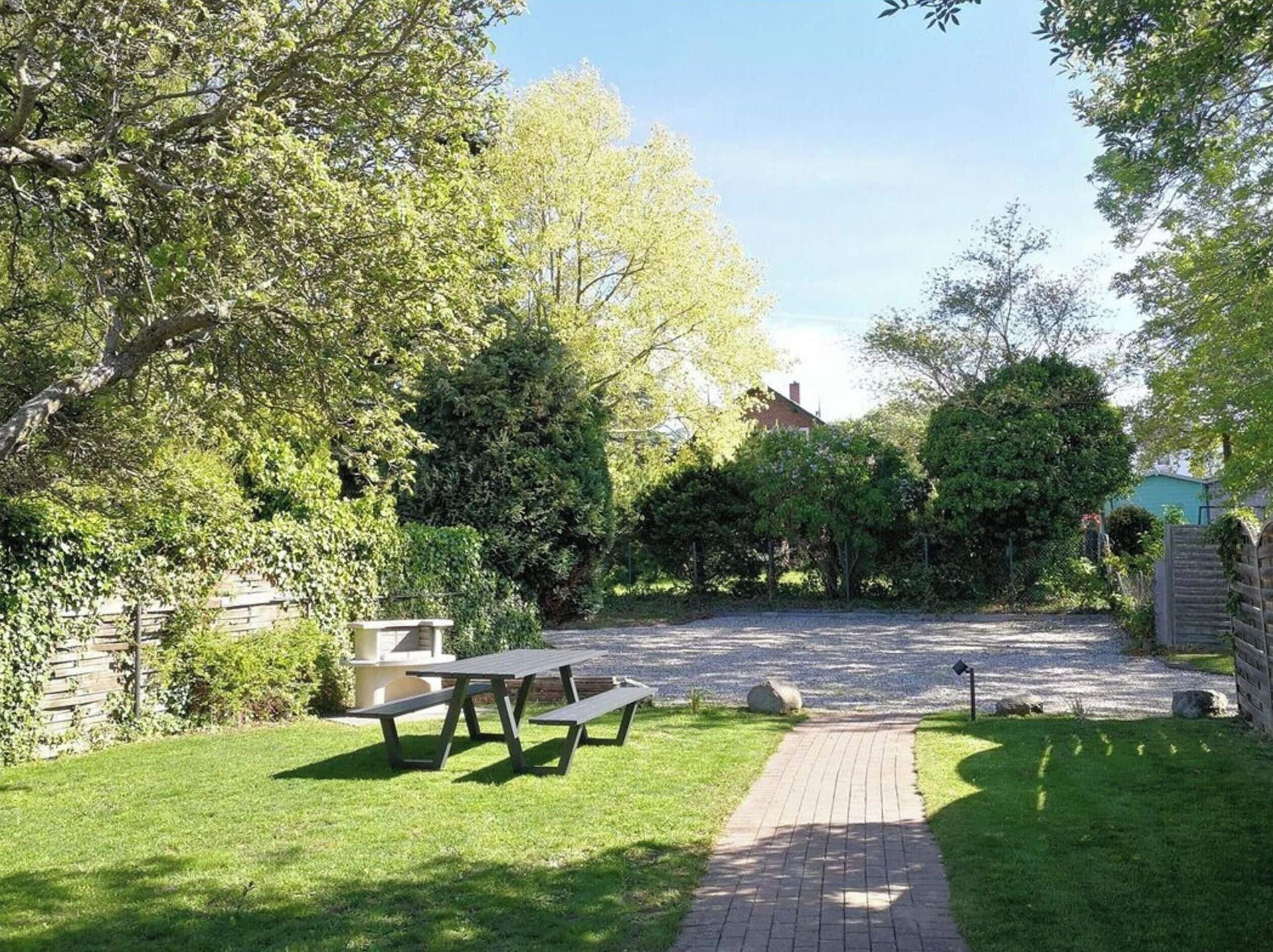A picnic area with benches, a paved path, and a house in the background.