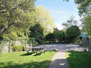A picnic area with benches, a paved path, and a house in the background. - Country House on the Riverbank, Apartment 1 (Heiligenhafen)