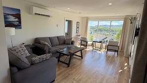 Ein modernes Wohnzimmer mit einem grauen Sofa, einem Couchtisch und Blick auf eine Stadtkulisse durch große Fenster.