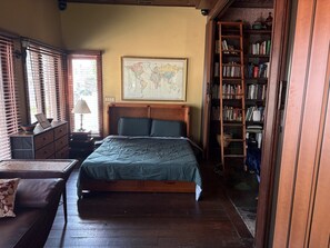 Ein Schlafzimmer mit einem Bett, einem Schminktisch, einer Karte an der Wand und einem Bücherregal.
