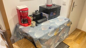A small kitchen area with a coffee maker, a microwave, and a table covered with a leaf-patterned tablecloth. - ROOM FOR RENT FOR 2–3 PEOPLE (Saint-Hilaire-de-Riez)