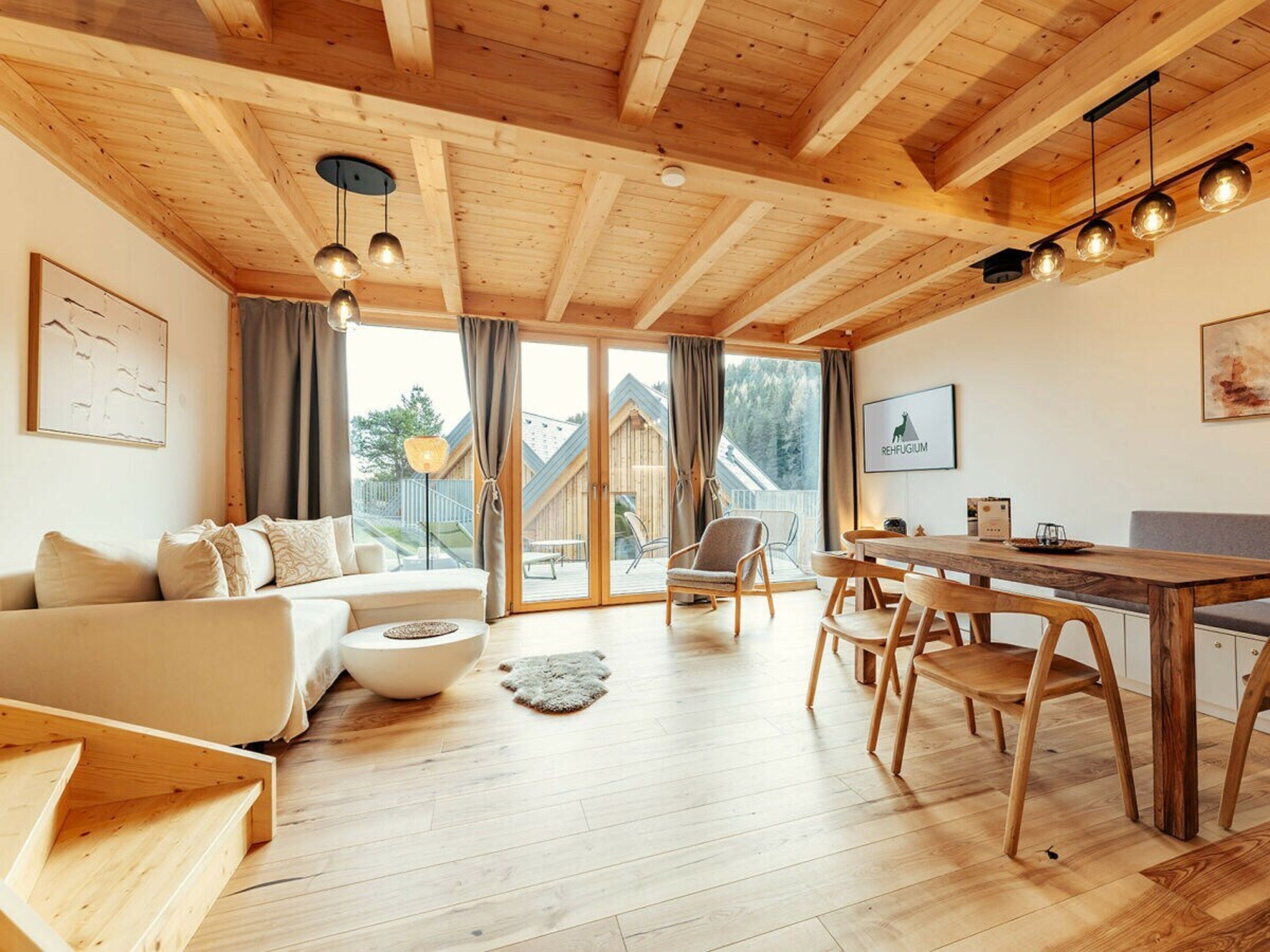 A cozy living room with a wooden ceiling, a sofa, a dining table with chairs, and a fireplace.