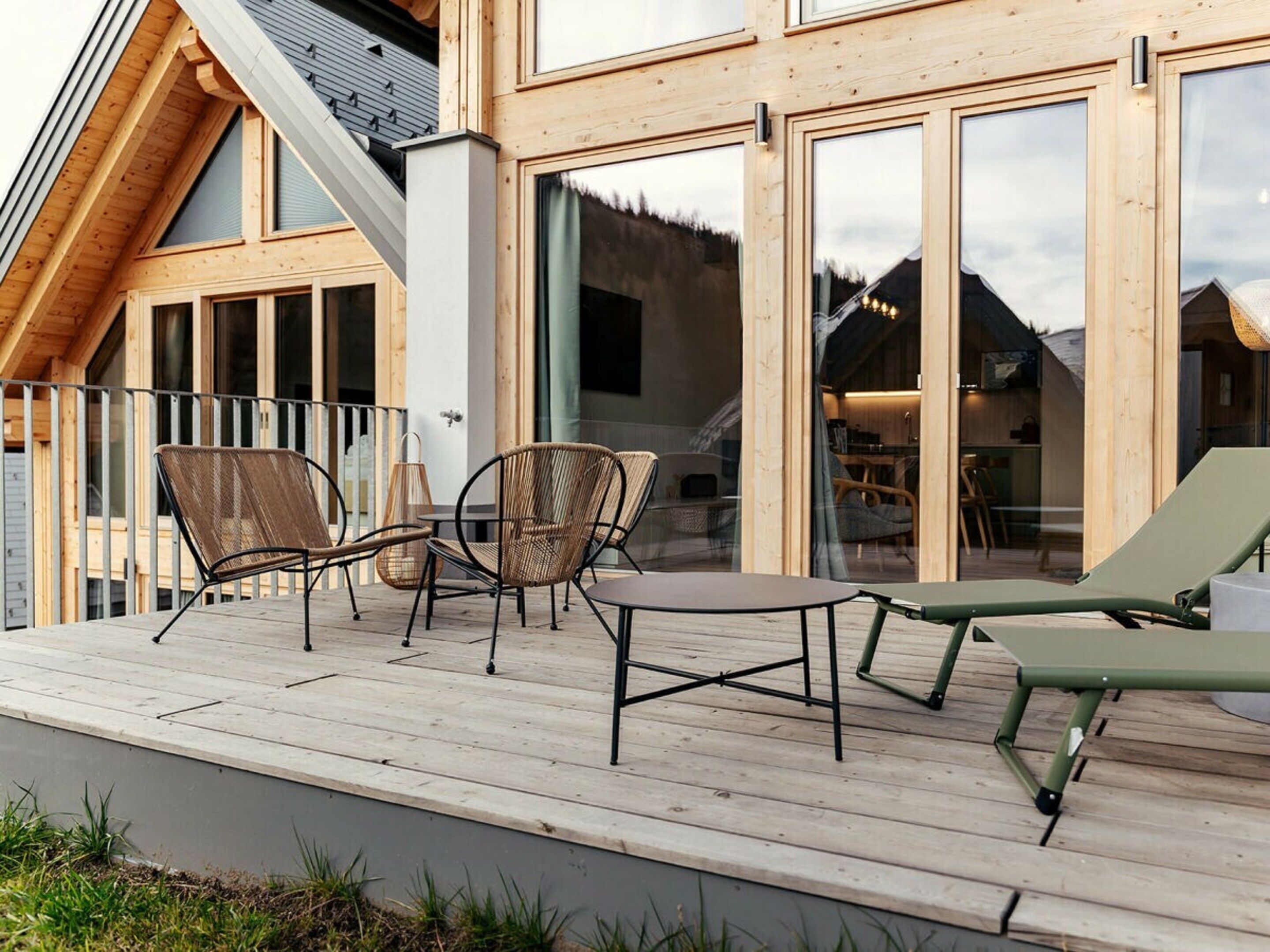 Una terraza de madera con mobiliario exterior, ventanas amplias y vistas a las montañas.