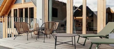 A wooden deck with outdoor furniture, large windows, and a view of the mountains.