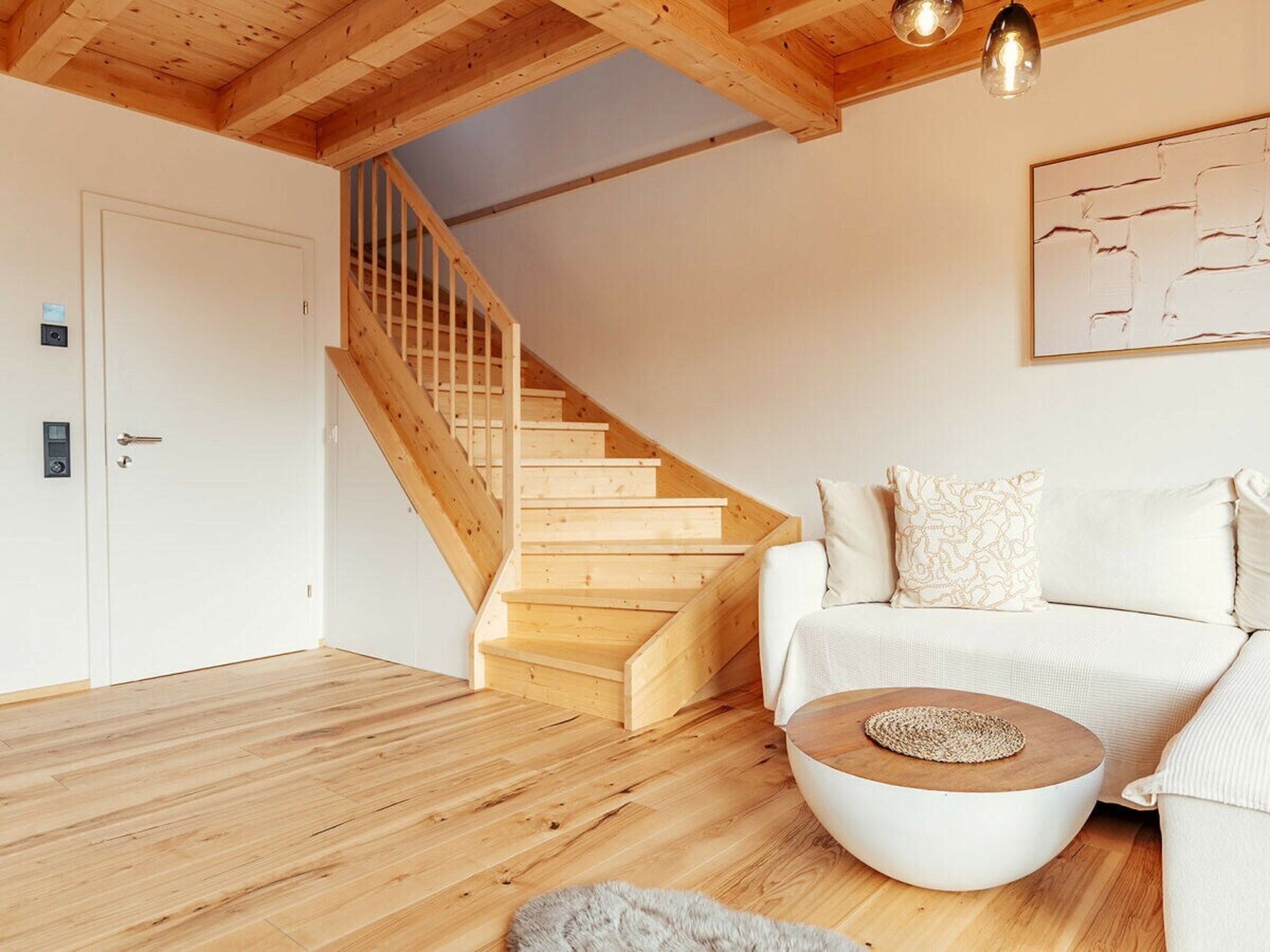 Ein modernes Wohnzimmer mit einer Holztreppe, einem weißen Sofa und einem runden Couchtisch.