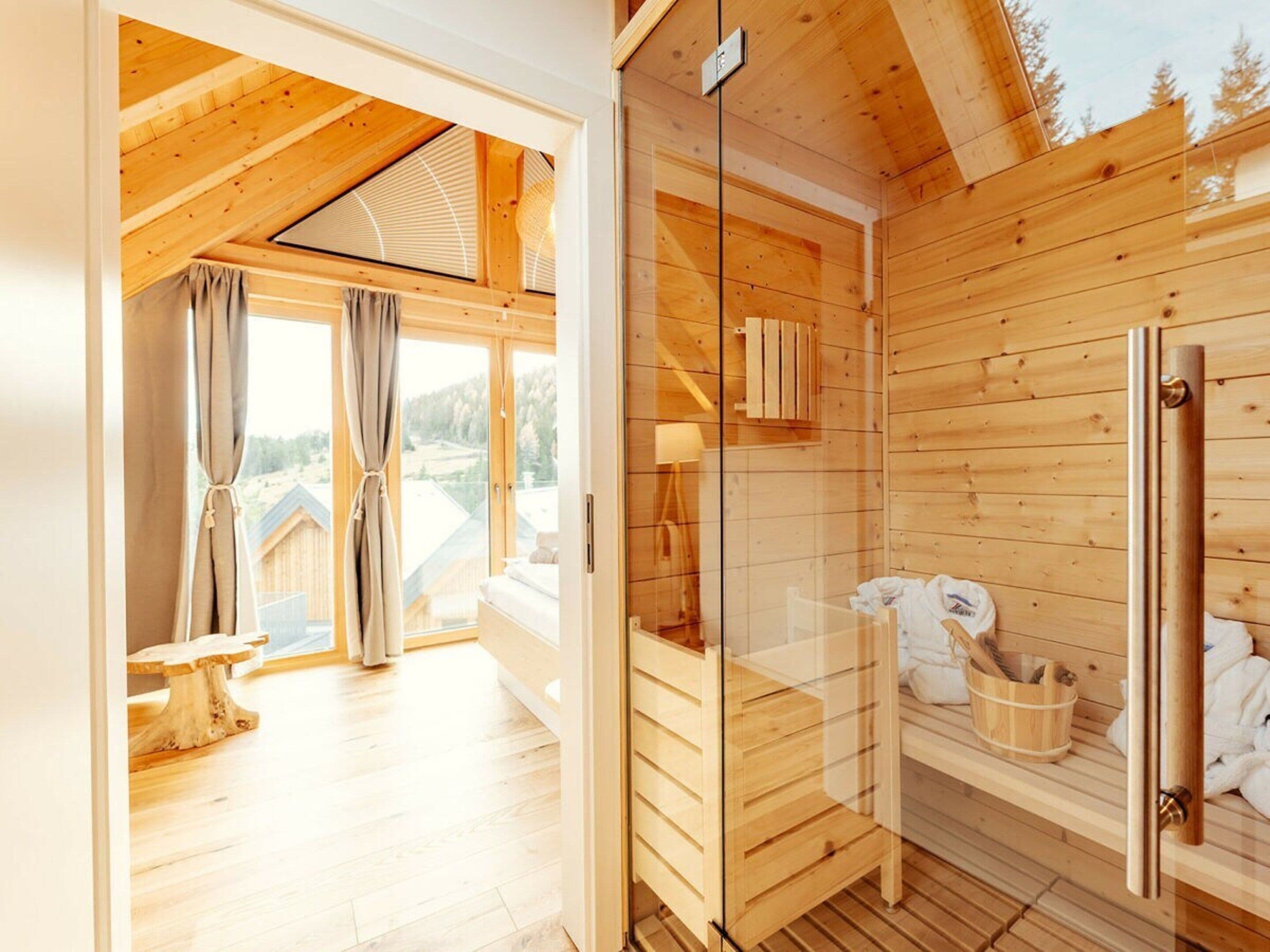 Innenansicht einer Holzhütte mit Duschkabine aus Glas, einer hölzernen Bank und Blick ins Freie.