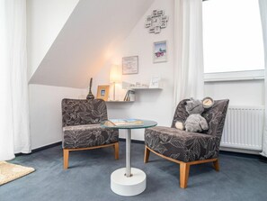 Une pièce comprenant deux fauteuils à motifs, une petite table en verre, une lampe et un mur orné de tableaux encadrés.