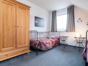 Une chambre à coucher avec un lit, une armoire, une petite table, une fenêtre avec des rideaux et un radiateur.