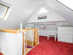 Une chambre d’enfant avec un lit superposé, une petite table, une commode et une fenêtre donnant sur une route.