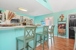 Une cuisine avec un mur d’accent de couleur turquoise, un four à micro-ondes, un réfrigérateur et deux tabourets de bar.