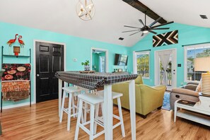 Une pièce avec un mur de couleur turquoise, une porte noire, un ventilateur de plafond et un coin repas comprenant une table et des chaises.