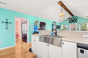 A kitchen with a large island, white cabinets, a stainless steel sink, and a ceiling fan. - Beach Walk: Dog-friendly Home Near Scenic Beach Walkover (Oak Island)