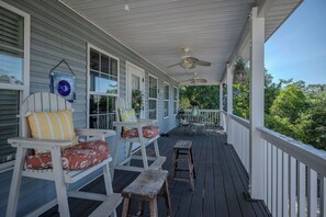 A covered porch with white railings, two rocking chairs with cushions, a small table, and a ceiling fan. - Beach Walk: Dog-friendly Home Near Scenic Beach Walkover (Oak Island)