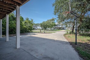 A residential area with a covered patio, a concrete driveway, and houses in the background. - Beach Walk: Dog-friendly Home Near Scenic Beach Walkover (Oak Island)