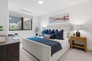 Quarto moderno com uma cama grande, mesa de cabeceira, escrivaninha e janela com vista para rochas.