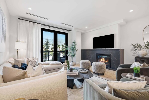 A modern living room with a fireplace, comfortable seating, and a large window offering a view of the outdoors. - Frontgate 229 - 4 Bedroom Residence (Avon)