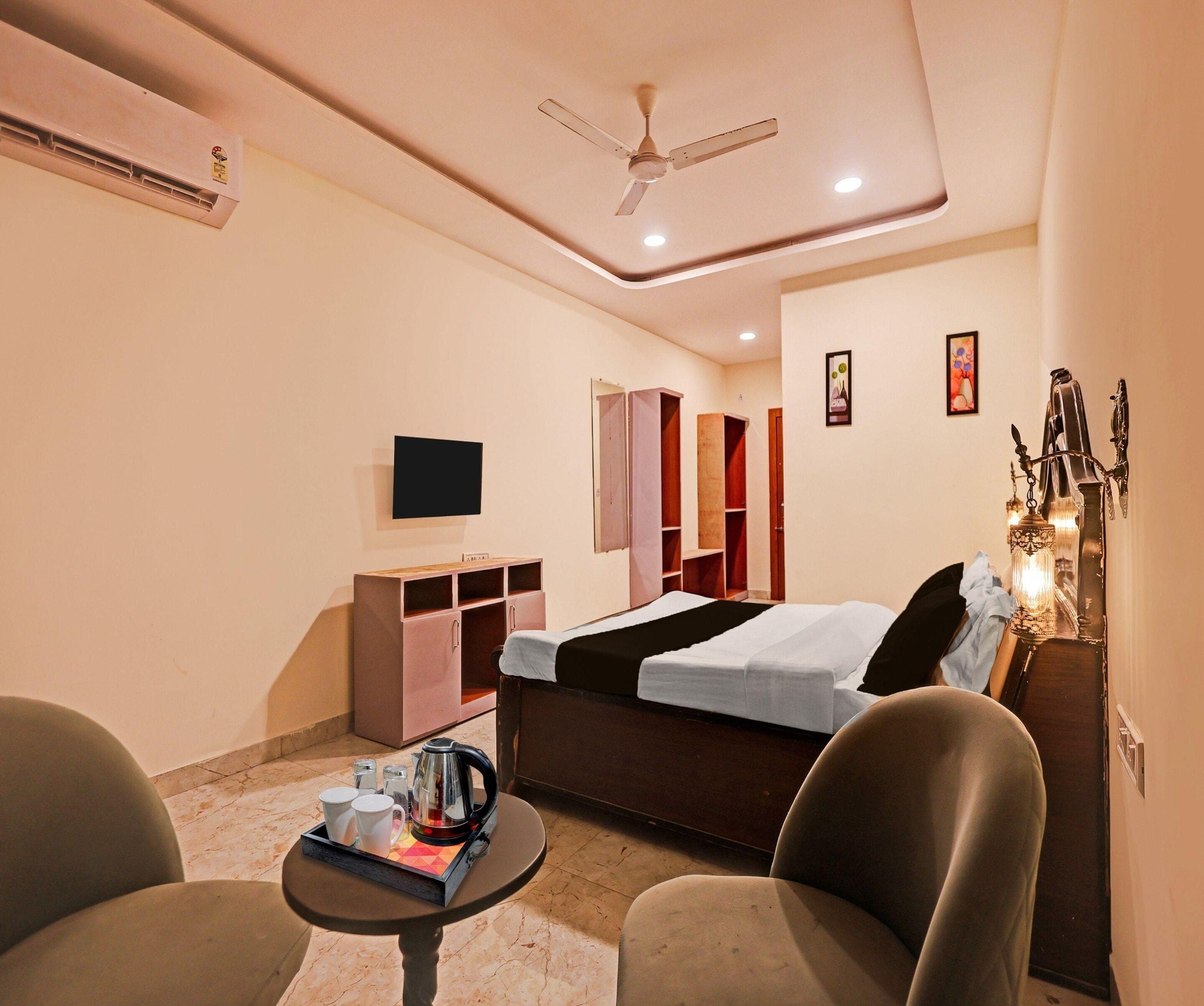 A hotel room with a bed, a television, a ceiling fan, a small table with a tray of items, and a decorative wall piece.