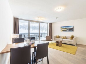Ein modernes Wohnzimmer mit Essbereich, großen Fenstern, einer Couch und einem Bild an der Wand.