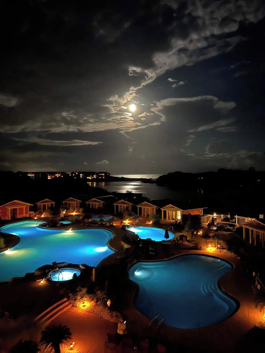 A resort with multiple swimming pools, a moonlit sky, and a view of the sea.