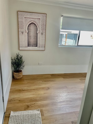 A room with a wooden floor, a framed artwork depicting an ornate door, a potted plant, and a window with a view of buildings.