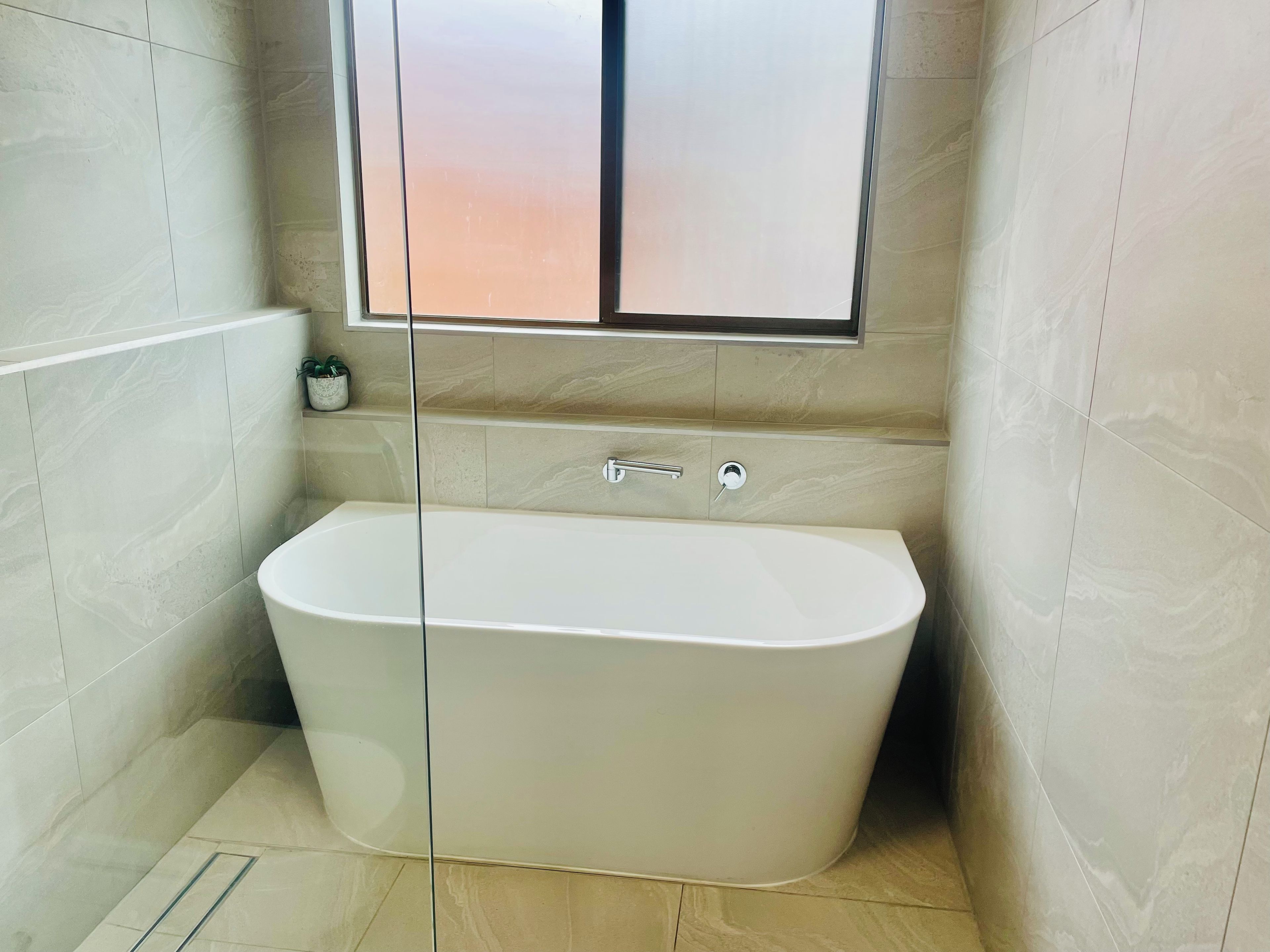 Ein modernes Badezimmer mit einer freistehenden Badewanne, einer Duschkabine aus Glas und einem kleinen Topfpflanzen an der Wand.