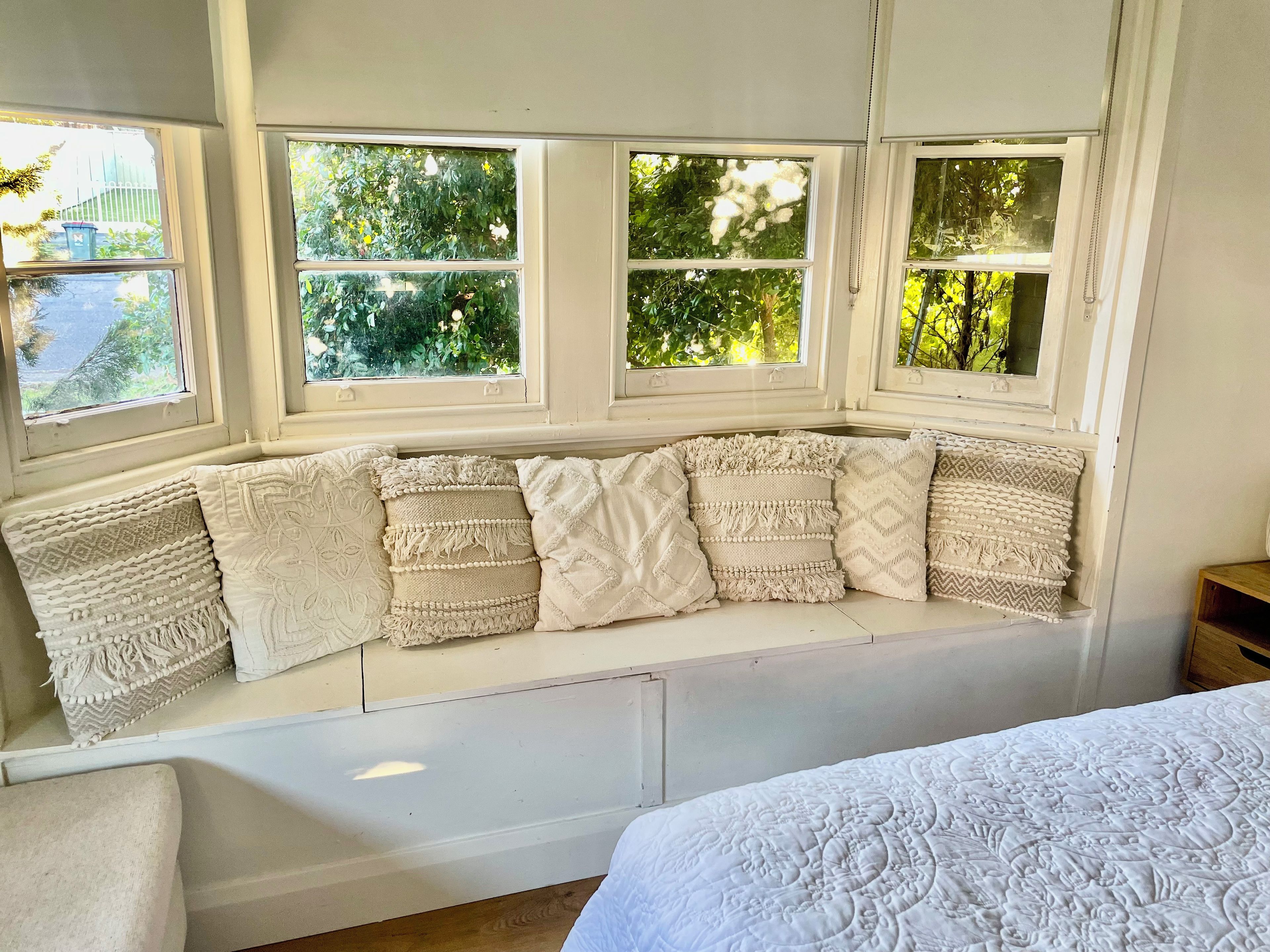 A room with a built-in bench along a window with multiple panes, offering a view of greenery outside.