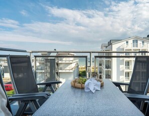 A balcony with a table set for dining, overlooking a residential area with modern buildings. - Holiday Apartment With 1 Bedroom (Grossenbrode)