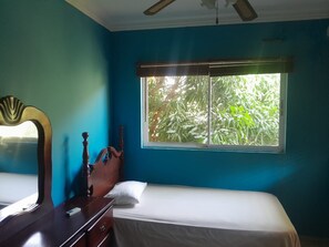 A room with a bed, a dresser, a mirror, and a window with a view of greenery.