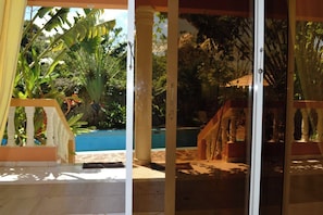 A covered outdoor area with a pool, palm trees, and a wooden structure.