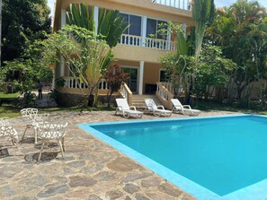 A swimming pool with lounge chairs, a stone patio, and a building with a balcony.