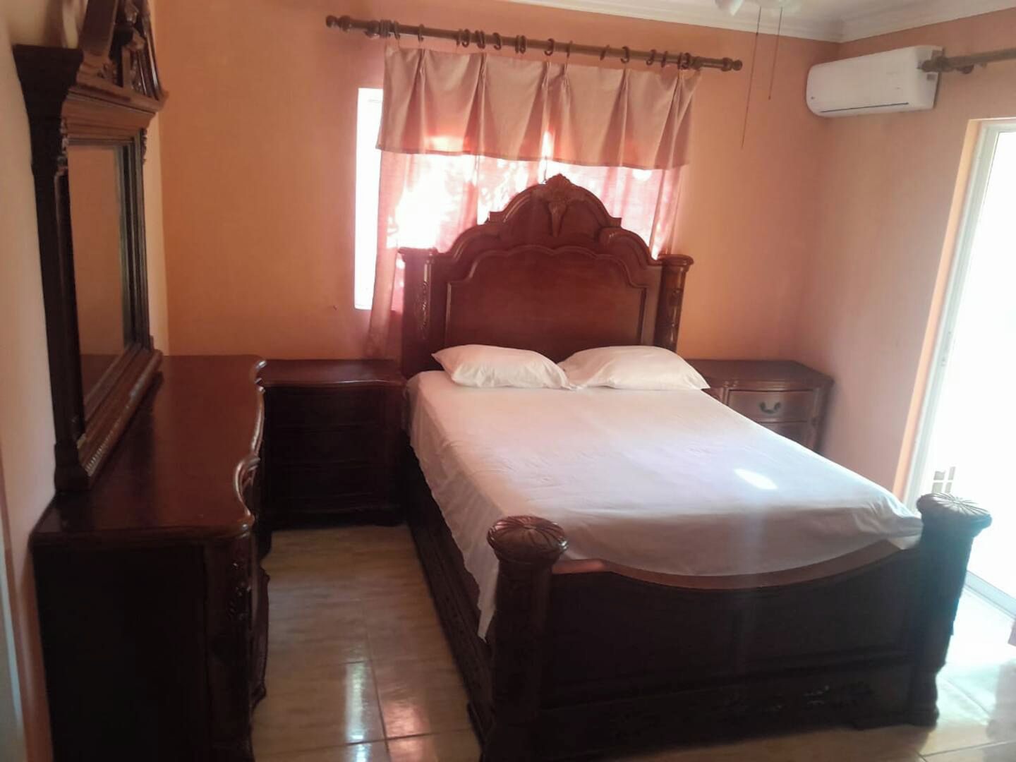 Un dormitorio con una cama de madera, una mesita de noche, un aparador y una ventana con cortinas.