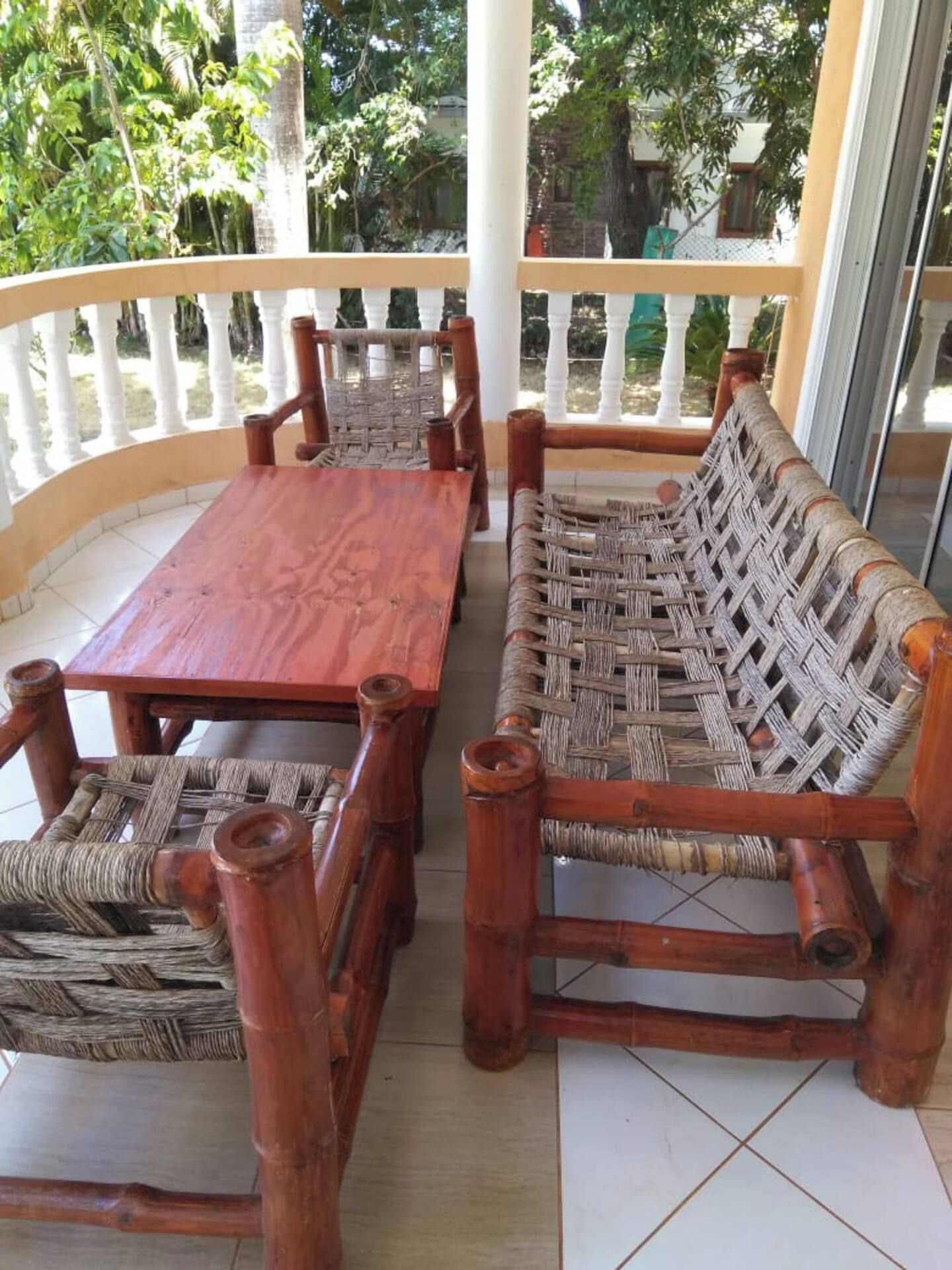 Un conjunto de banco y mesa de madera en un balcón con barandillas blancas, rodeado de follaje.