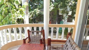 A wooden bench and table set on a balcony with white balustrades, surrounded by greenery.