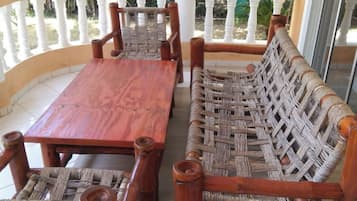 Un conjunto de banco y mesa de madera en un balcón con barandillas blancas, rodeado de follaje.