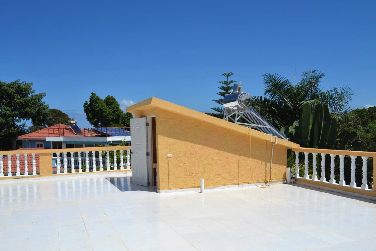 Un amplio espacio exterior con piso de baldosas blancas, pared amarilla y estructura metálica.