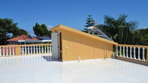A spacious outdoor area with a white tiled floor, a yellow wall, and a metal structure.