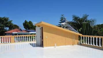 Un amplio espacio exterior con piso de baldosas blancas, pared amarilla y estructura metálica.