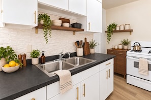 Cozinha moderna com armários brancos, bancada preta, pia de a ço inoxidável e fogão branco.