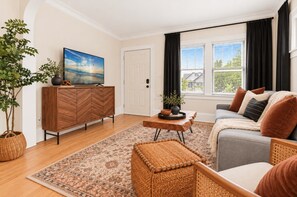 Uma sala de estar com um aparador de madeira com padrão herringbone, uma televisão, um sofá com almofadas, uma mesa de centro e um tapete estampado.