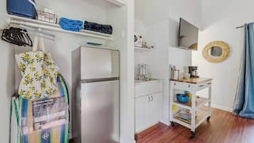 Eine kompakte Küche mit Kühlschrank, Mikrowelle und einem kleinen Spülbecken. Es gibt einen Holzkasten und einen kleinen Tisch mit Wasserkocher und Tassen.