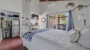 Et soveværelse med seng, garderobeskab, tekøkken og en balkon med gardiner.
