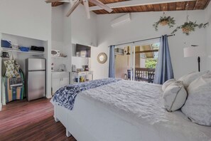 Une chambre avec un lit, une armoire, un coin cuisine et un balcon avec des rideaux.