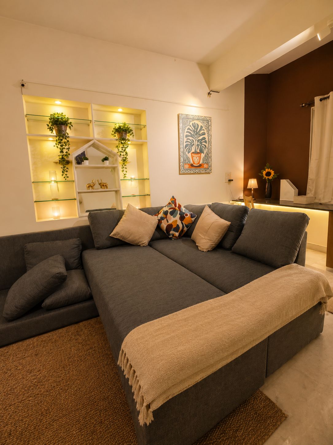 A modern living room with a grey sofa, a beige throw blanket, and a wall-mounted shelf with plants.